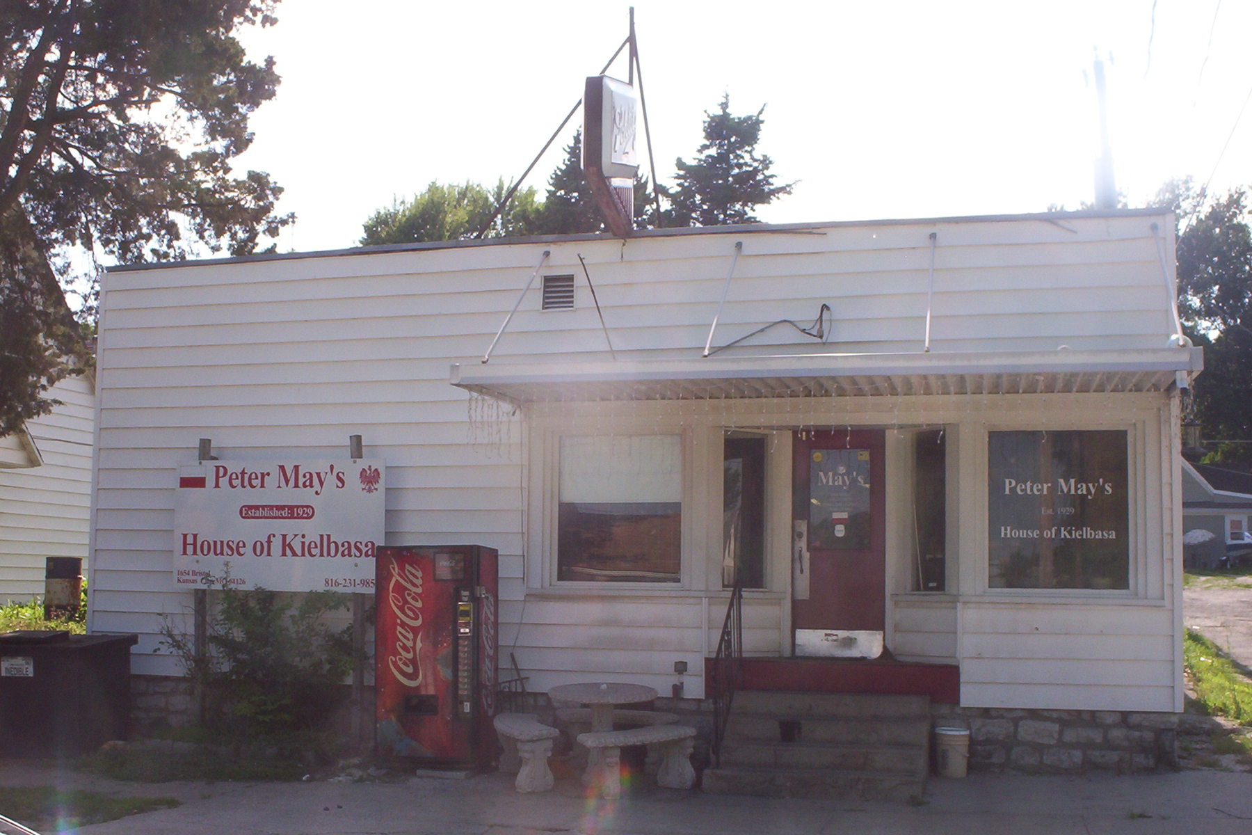 A tiny ramshackle filthy-white-clad corner store with a sign that says “Peter May’s House of Kielbasa, established 1929”