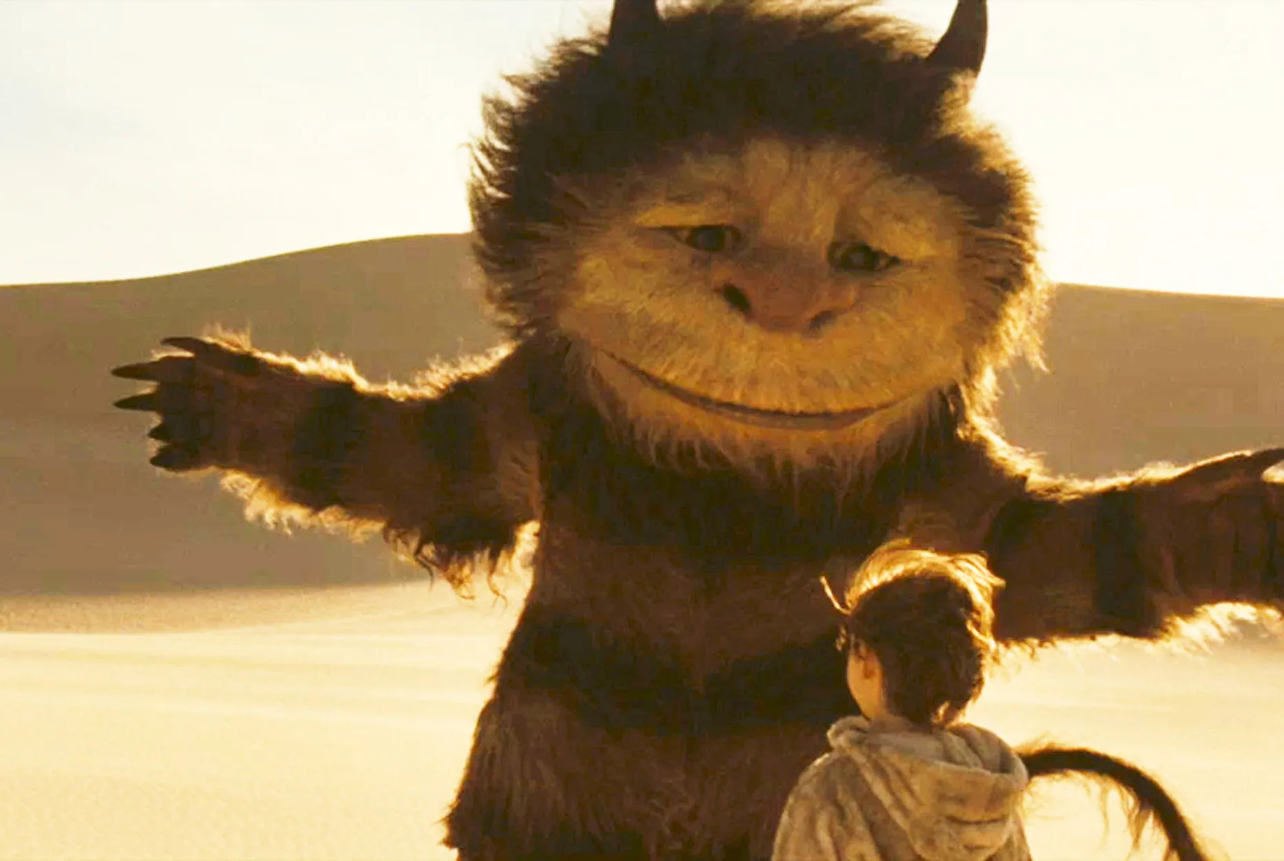 A still shot from the movie WHERE THE WILD THINGS ARE with a very large monster looming in an instructive manner over a small boy dressed in a tiger costume.