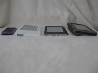 Four e-reading devices lying on a white cloth to compare thickness. From left to right, Blackberry, Kindle keyboard, Sony e-Reader, eBookwise