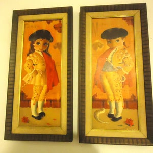 Two small framed prints of big-eyed dolls/children dressed up as Spanish matadors, with their “swords” being candy canes.