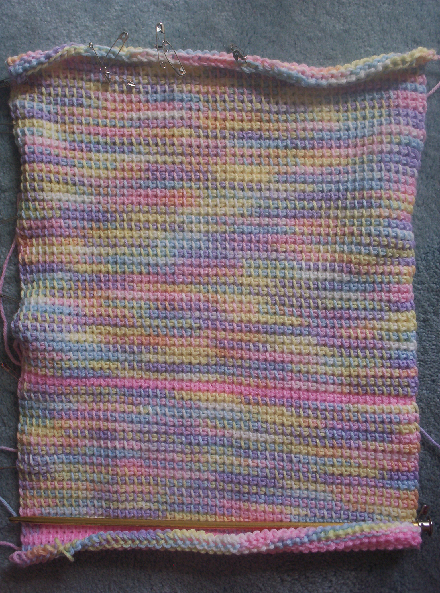 A swatch of Tunisian crochet of pastel variegated ombré acrylic yarn.