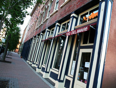 A brick sidewalk in front of a row of shops of 19th-century brick buildings.
