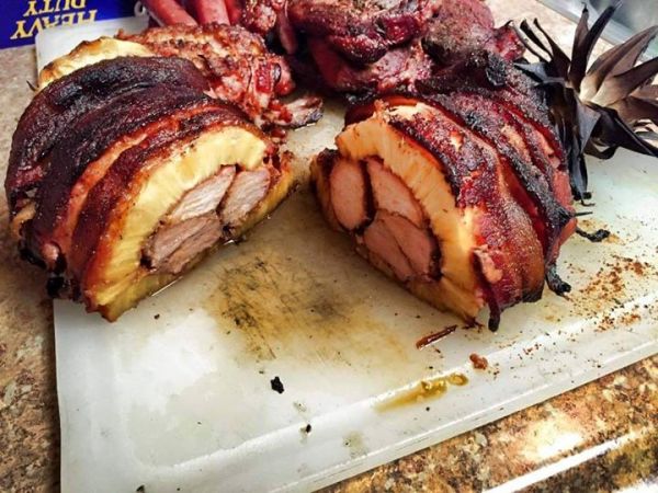 An image of a nicely presented dish of pork ribs stuffed in a hollowed-out pineapple wrapped in bacon.