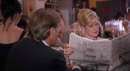 A still shot of Melanie Griffith (Billie Dawn) and Don Johnson (Paul Verrall) at the dinner table while Billie reads the newspaper.