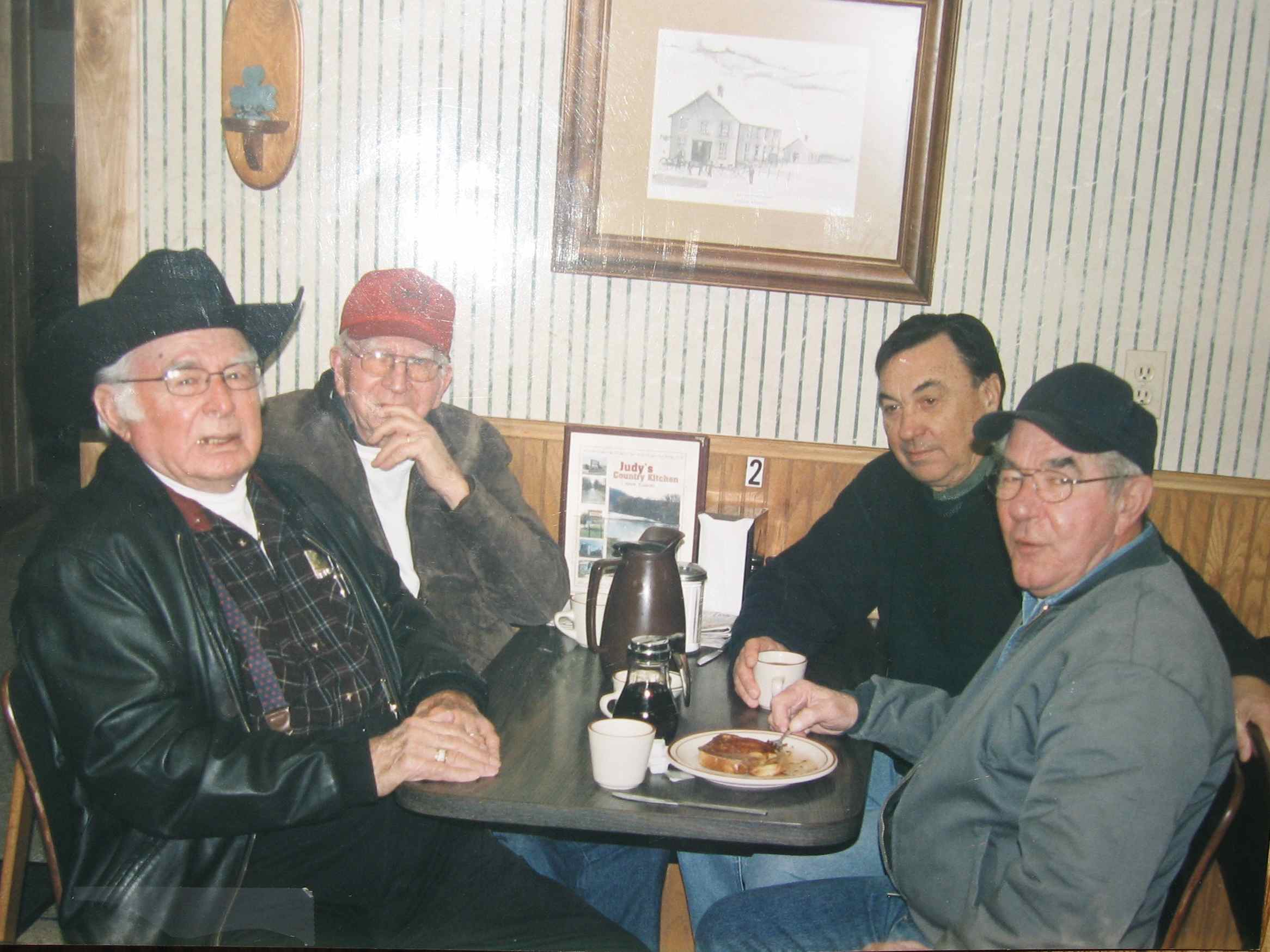Four old men sitting in an old café eating breakfast.