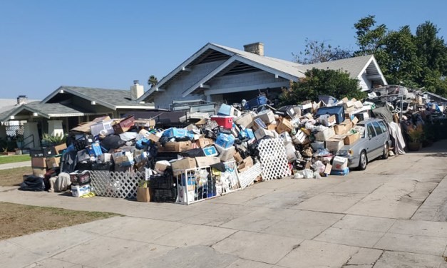 A garbage pile in front of and spilling over into the driveway of a relatively nice house.