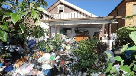 A garbage pile in the front yard of a dilapidated house.